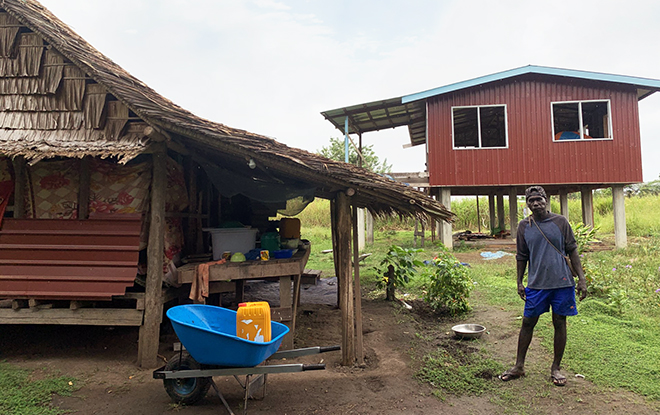 A farmer showing his current house (left) and new hourse being built (at the rear).