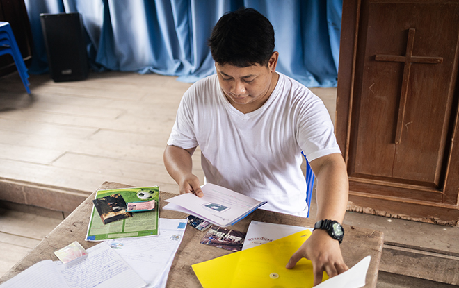 Anurak is looking through his books, files, photos and sponsor’s letters that he kept. He is sitting inside the chapel where he used to participate in Compassion program activities.