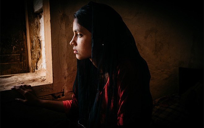 Young girl looking out of window with a sombre expression